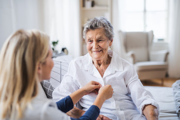 a health visitor helping a sick senior woman sitting on bed at home.