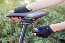  Black Saddle Against A Street Background.  The Hand With The Multitool Twists The Mount On The Seat.
