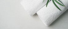 Spa Concept: Two White Fluffy Towels Twisted Into Rolls On A Light Surface With A Palm Leaf With Copy Space, Flat Lay