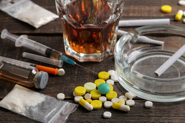 various addictive drugs including alcohol, cigarettes, and drugs on a brown wooden table. drug addic
