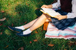 © twinsterphoto - Close-up of woman wearing school college uniform with scotland pleated skirt and reading a book in nature green grass park.