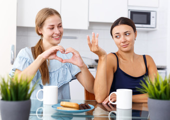 Young smiling girlfriendsshowing the heart with hands during drinking tea at table