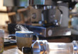 © Natsicha - close up a ceramic cup of hot smoke coffee on wooden table with blurred coffee machine in background