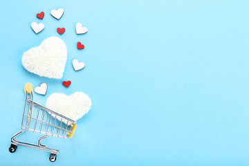 Shopping cart with rope and wooden hearts on blue background