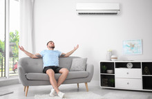 Young Man Relaxing Under Air Conditioner At Home