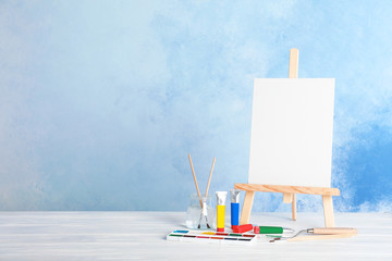 Wall Mural - Wooden easel with blank canvas board and painting tools for children on table near color wall. Space for text