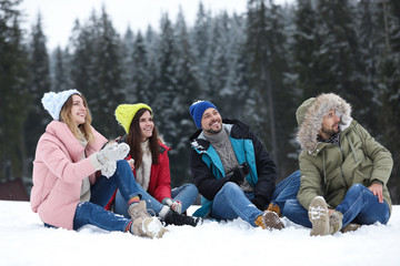 Wall Mural - Group of friends sitting on snow outdoors. Winter vacation