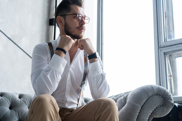 Wall Mural - Enjoying free time. Thoughtful young man in full suit looking away while sitting on the sofa at home.