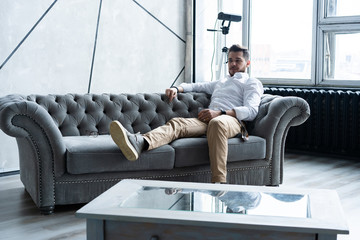 Wall Mural - Feeling lonely. Stylishly dressed young man holding a glass while sitting on sofa.