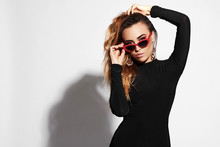 Close Up Portrait Of Pretty Young Woman In Black Stylish Dress With Glasses Against White Background. Female Fashion Model Posing With Red Sunglasses