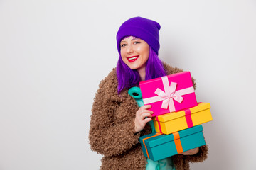 Wall Mural - Beautiful young girl with purple hair in jacket with holiday gift boxes on white background.