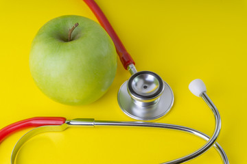 Green Apple with medical stethoscope isolated on yellow background for healthy eating. Selective focus and crop fragment. Healthy, Diet and copy space concept