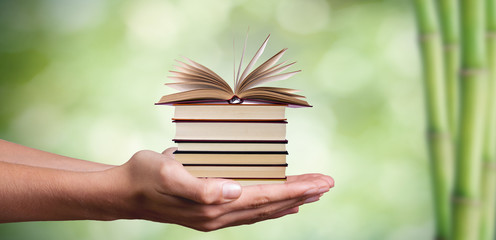 hands with stacked books and natural green background