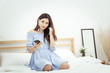 © asiandelight - A beautiful Asian woman with headphone relaxing at home , sitting on the bed listening to music from application on mobile phone