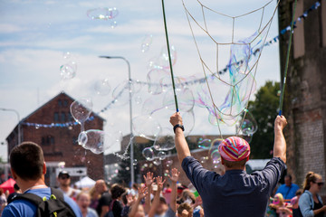 Wall Mural - A freelance clown blowing hundreds of tiny, small and big bubbles at outdoor festival in city center. Concept of entertainment, birthdays. Kids having fun. Shower of bubbles flying in the happy crowd