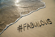 Fabulous, the fashionable catchphrase with a modern social media hashtag handwritten on a smooth sand beach with incoming wave