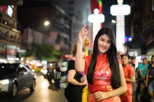 A Beautiful, Long-haired Thai Woman, An Asian Woman Wearing A Chinese Dress, Standing Smiling And Holding A Chinese Tassel At Roadside Chinatown, Yaowarat, Bangkok, Thailand At Night.