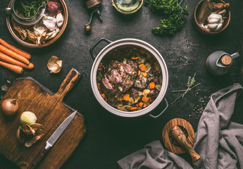 Sticker - Cooking preparation of stewed meat.  Roasted beef meat in cast iron cooking pot with vegetables on dark rustic background with kitchen utensils and seasoning, top view with copy space.