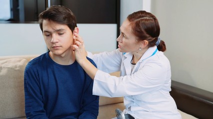 Woman doctor puts a hearing aid on a young guy.