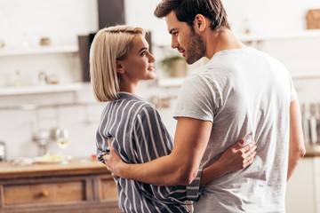 selective focus of handsome boyfriend and attractive girlfriend hugging and standing in kitchen