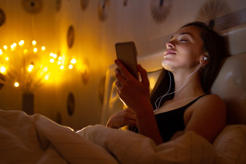 Young, attractive woman before bed listening and enjoying relaxing music after a hard, working day. Chatting online with friends