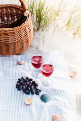 Two wine glasses, grapes, wicker basket on beach