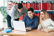 © Aleksandr - University students sitting together at table with books and laptop. Happy young people doing group study in library