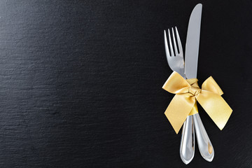 fork and knife with golden ribbon on slate tray