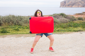 Wall Mural - People, travel and holidays concept - young woman is trying to lift her luggage up