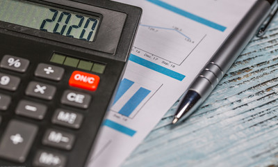 Calculator with 2020 digits lie on financial document with pen on the wooden table