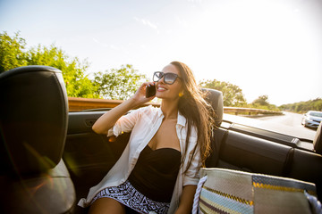 Wall Mural - Woman uses mobile phone and siting in cabriolet at summer day