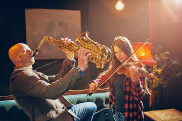 Two talented musicians playing violin and saxophone. Home studio interior.