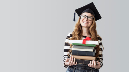 Young graduated student looking away and carrying books on gray background