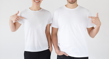 Wall Mural - Smiling young couple pointing at blank white t-shirts with index fingers, copy space for your advertising, isolated on gray background