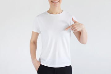 Wall Mural - Young woman smiling while pointing with index finger to white t-shirt, copyspace for advertising, isolated on gray background. No face photo