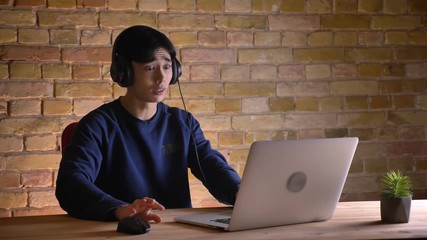 Closeup portrait of young attractive korean male student in headphones checking on the laptop and getting upset and frustrated.