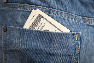 Paper money dollars stick out of jeans pocket.