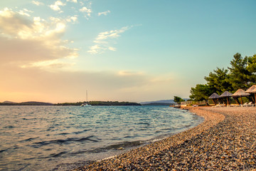 Wall Mural - Pebble beach at sunset. The yacht sails along the islands