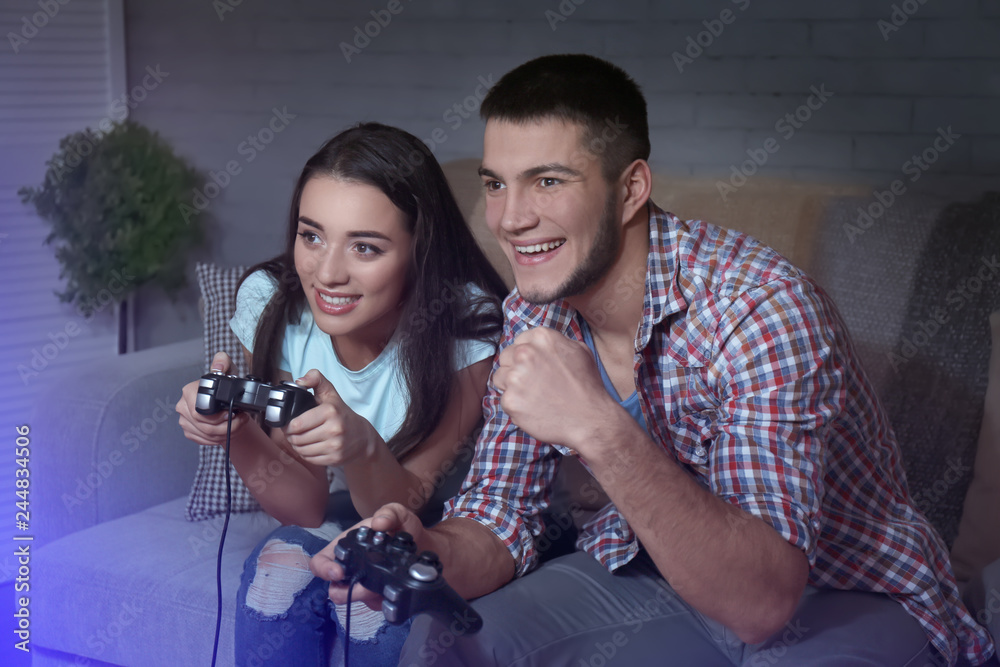 Emotional couple sitting on sofa and playing video game at home
