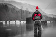 Black, White & Red Photo of a Man Fly Fishing in a Christmas Santa Hat - Wearing a Red Jacket and Waders, with Trees and Mountains in the Background in the Pacific Northwest on a Cloudy Winter Day