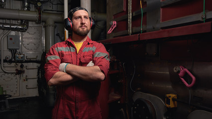 Ship mechanic staying near main engine in engine room.