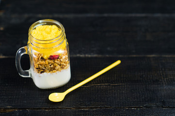 Wall Mural - muesli and yogurt with mango smoothie in glass mason jars, black background, space for text