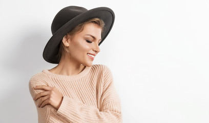 Portrait of charming gentle girl in cozy beige knitted sweater and trendy hat posing and looking down. Modern fashion and autumn concept. Copy space in right side