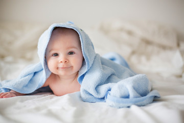 cute little baby boy, relaxing in bed after bath, smiling happily