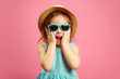 © Ilshat - Portrait of surprised girl with open moutn, wears in panama hat and sunglasses, expresses surprise and delight, stands over pink isolated background.