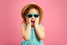 Portrait Of Surprised Girl With Open Moutn, Wears In Panama Hat And Sunglasses, Expresses Surprise And Delight, Stands Over Pink Isolated Background.