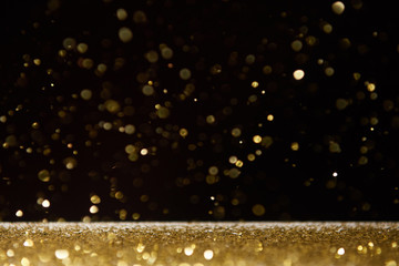 selective focus of golden shiny sparkles falling on table isolated on black