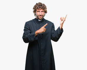 Canvas Print - Handsome hispanic catholic priest man over isolated background smiling and looking at the camera pointing with two hands and fingers to the side.