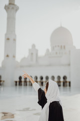 Wall Mural - Beautiful young woman in Arabic clothes pointed with hand at Sheikh Zayed Grand Mosque in Abu Dhabi.