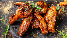 The Concept Of Indian Cuisine. Baked Chicken Wings And Legs In Honey Mustard Sauce. Serving Dishes In The Restaurant On A Black Plate. Indian Spices On A Wooden Table. Background Image.